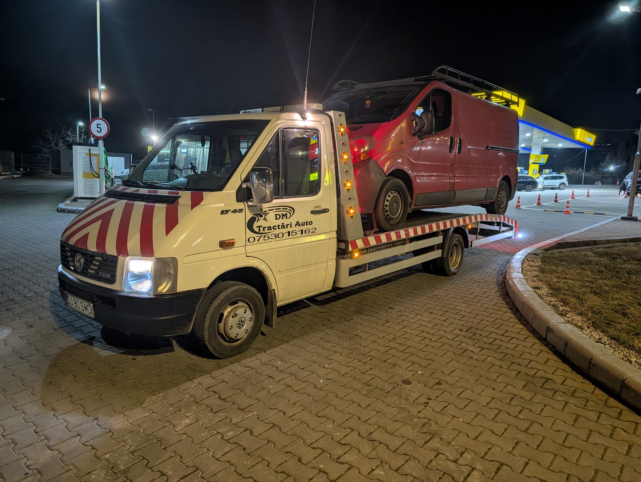 Autoturism roșu transportat pe platformă în timpul nopții